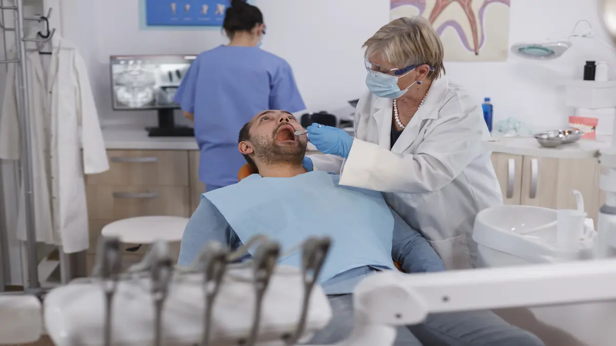 Dental professional in blue gloves closely inspecting a patient's infected tooth, looking for signs of abscess or decay.